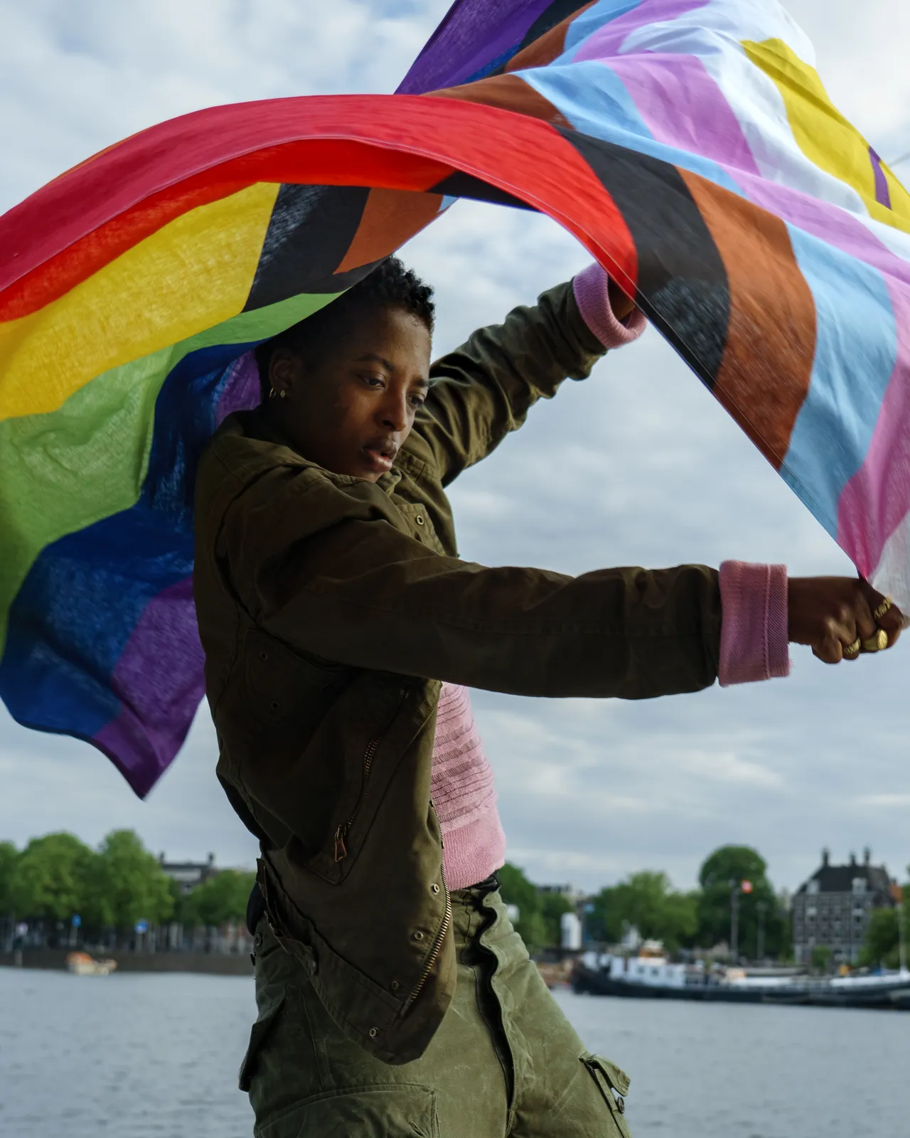 Iemand houdt de Intersex Progress Pride vlag boven het hoofd terwijl die opbolt in de wind aan het water