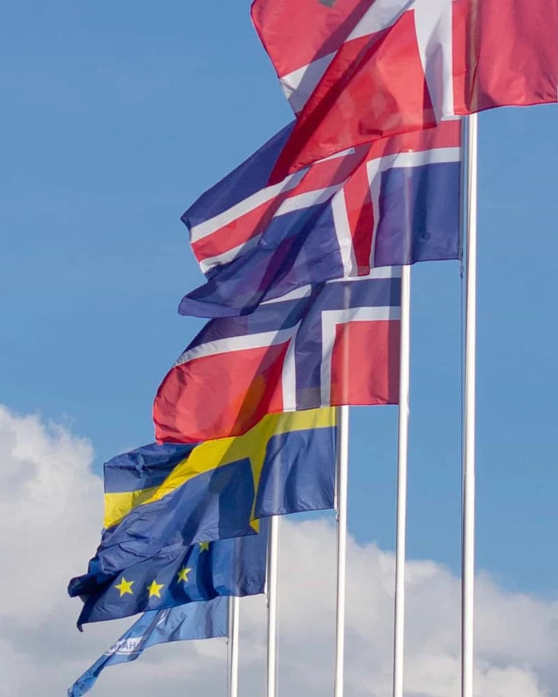 Noorse vlag wappert in een rij Noordse vlaggen aan witte masten tegen een blauwe lucht