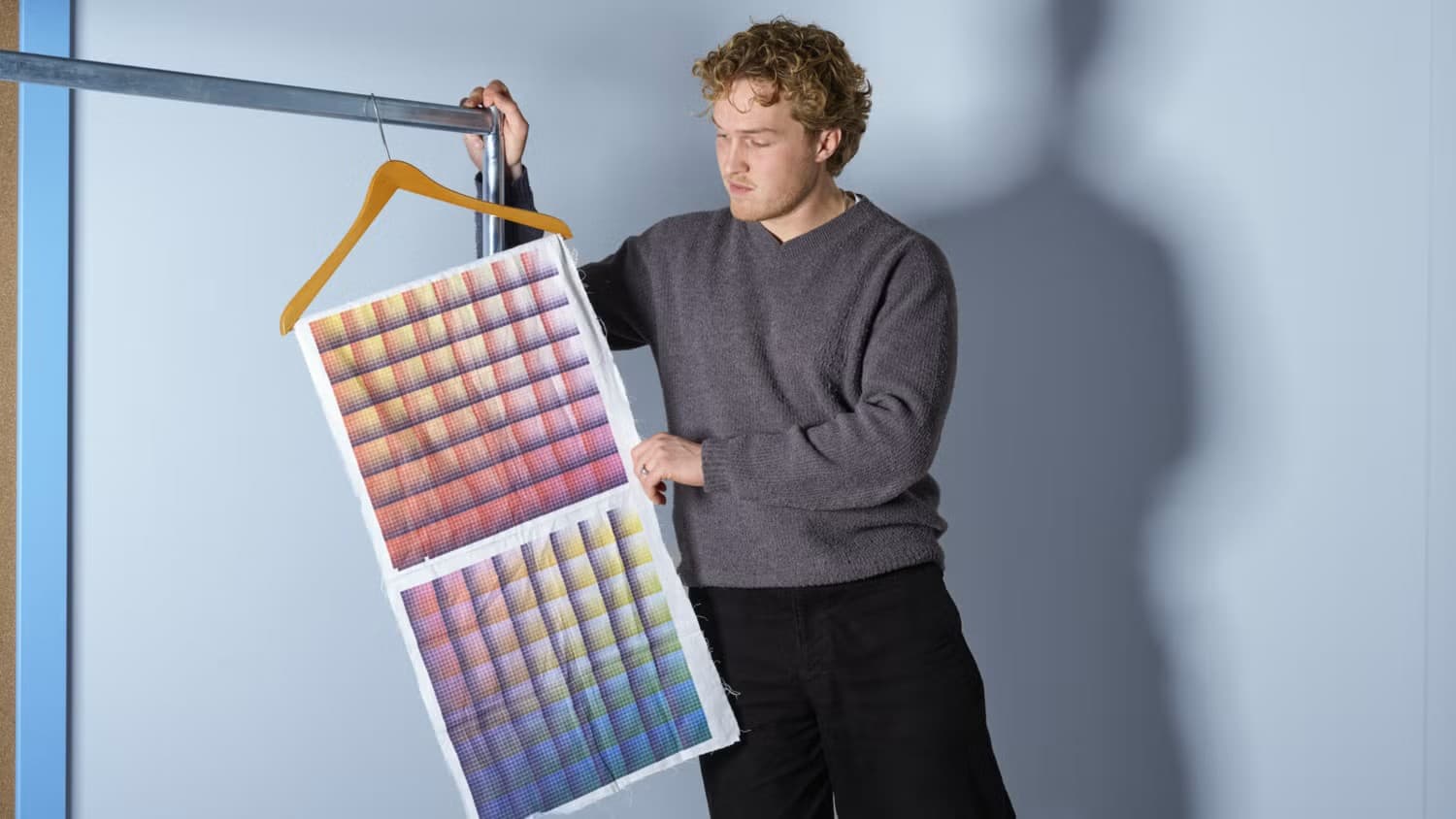 Man in a grey sweater holding up a printed fabric colour chart on a clothes hanger