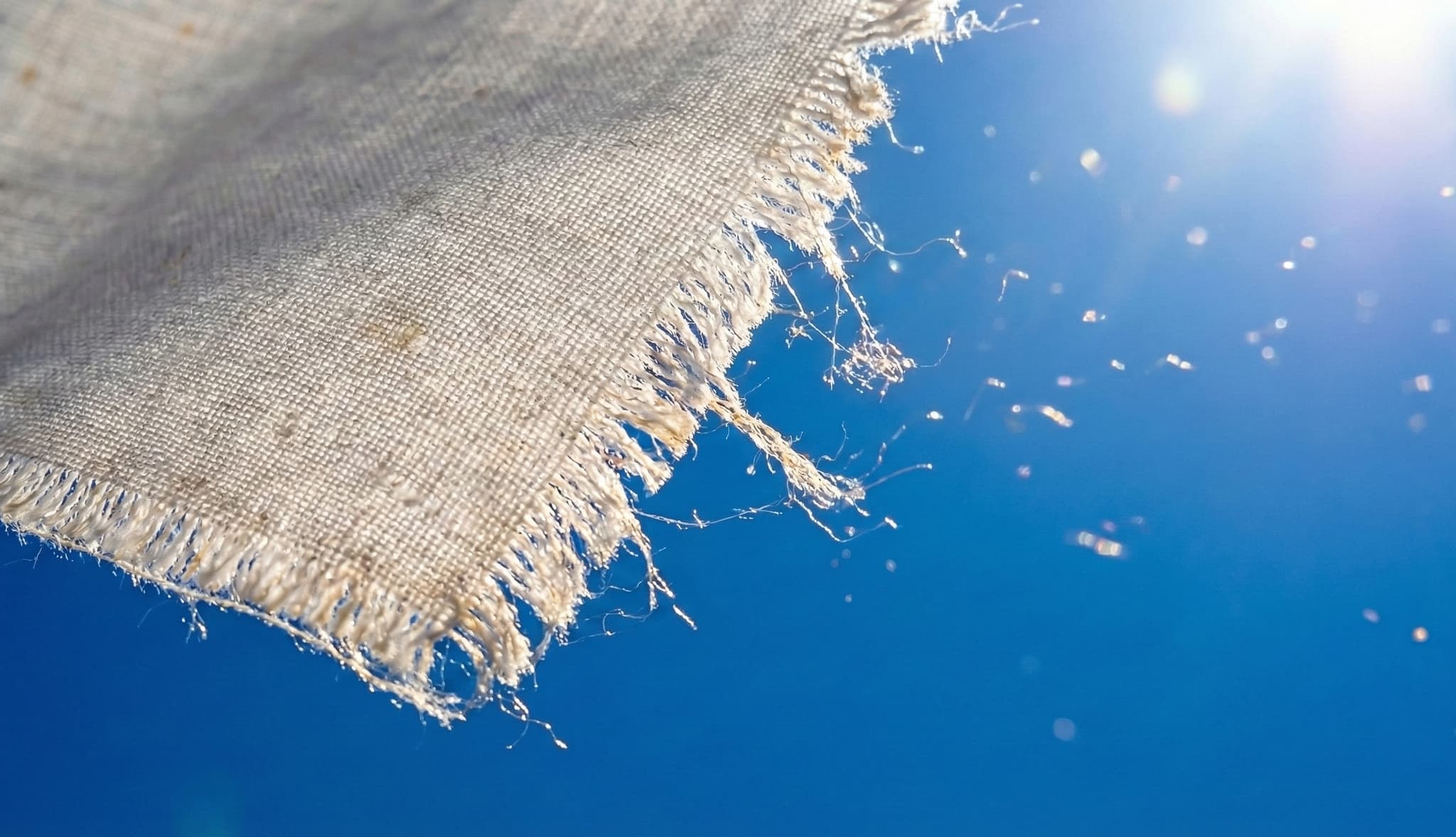 Gerafelde rand van een geweven vlag die losse vezels verliest tegen een blauwe lucht