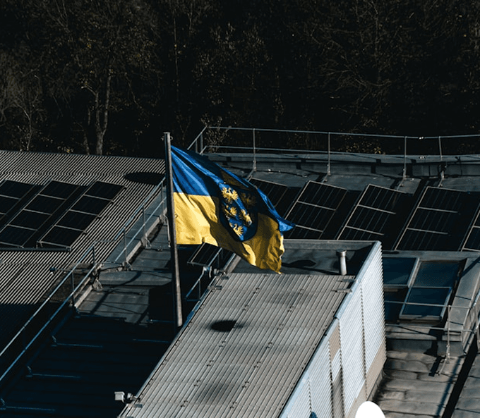 Blauw-gele vlag met een wapen wappert op een dak naast zonnepanelen