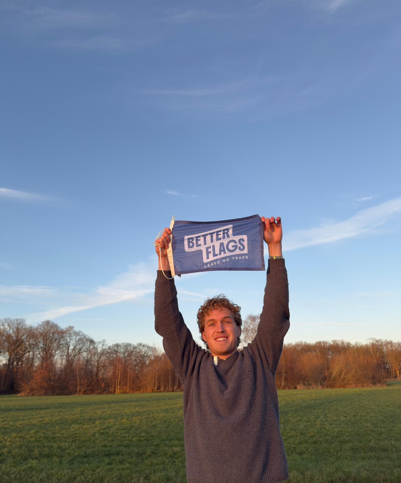Lachende man houdt een blauwe vlag van Better Flags boven zijn hoofd in een grasveld
