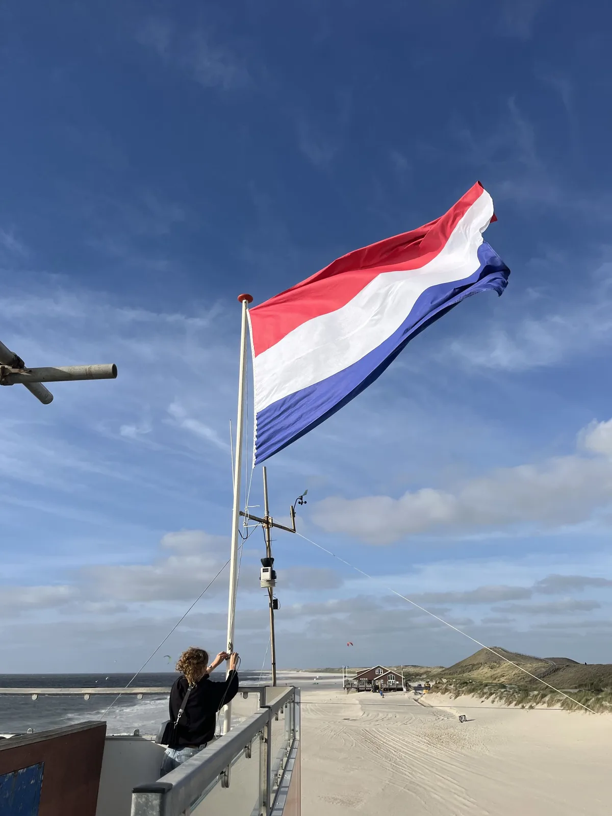 The Dutch national flag being hoisted on a mast at a North Sea beach pavilion