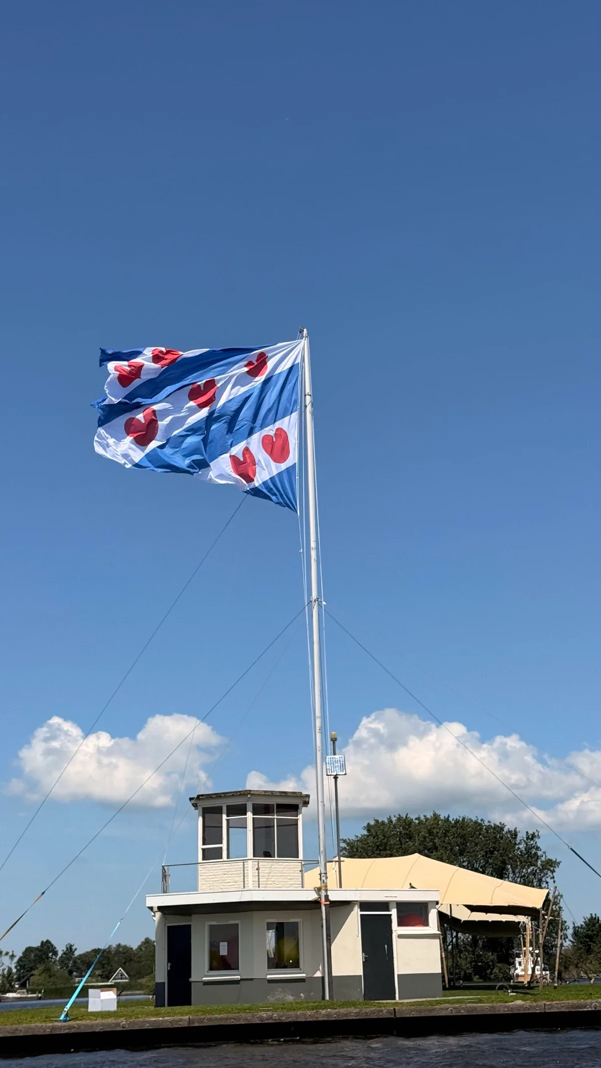 The Frisian flag flying from a tall white mast beside a waterway